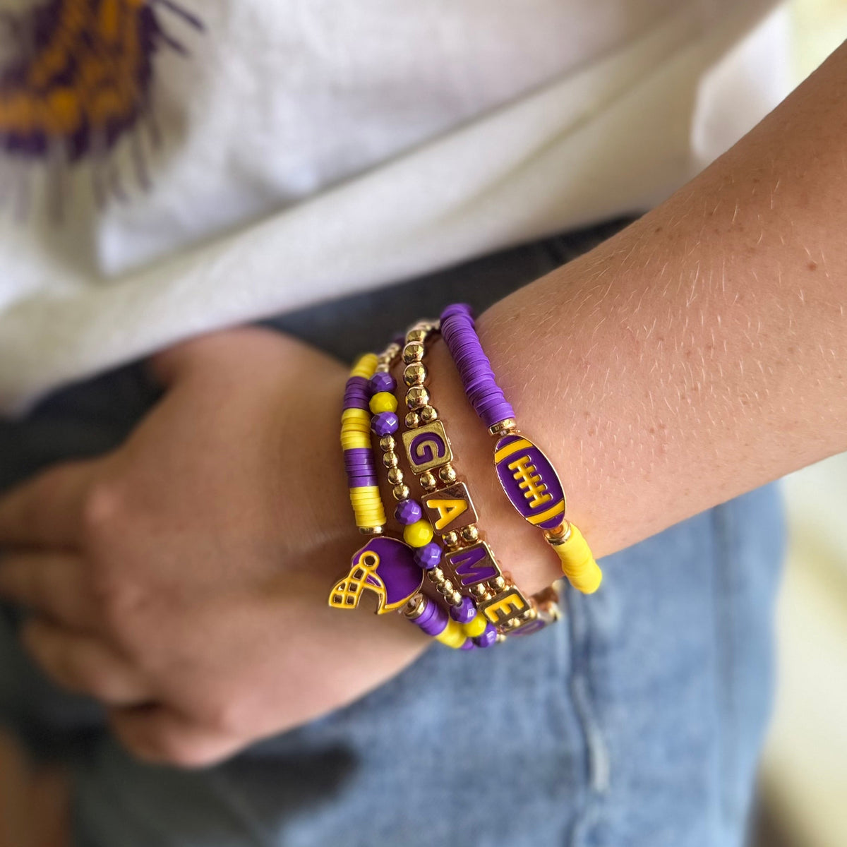Purple and gold beaded bracelet stack with football charms and enamel letter blocks, view 2